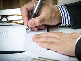 Mężczyzna składający podpis na dokumencie, w tle na biurku inne dokumenty i okulary