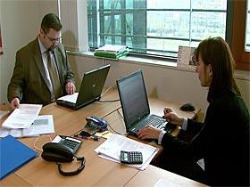 Kontrolerzy NIK przy pracy (mężczyzna i kobieta siedzący przy biurkach używający komputerów przenośnych i przeglądający dokumenty)