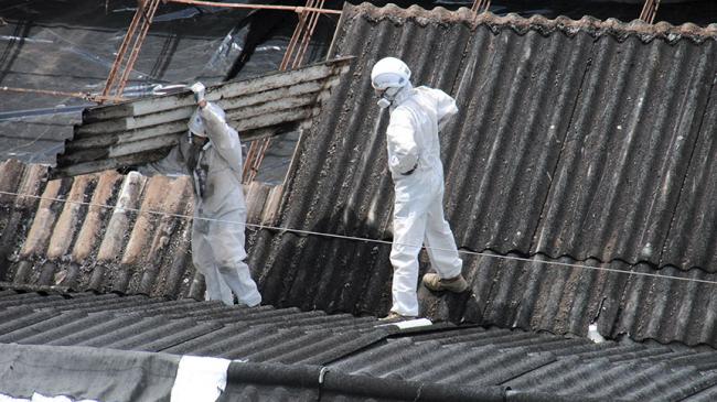 Dwóch robotników w kombinezonach usuwa azbest z dachu