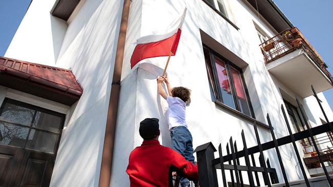 Ojciec asekuruje dziecko wieszające flagę na budynku